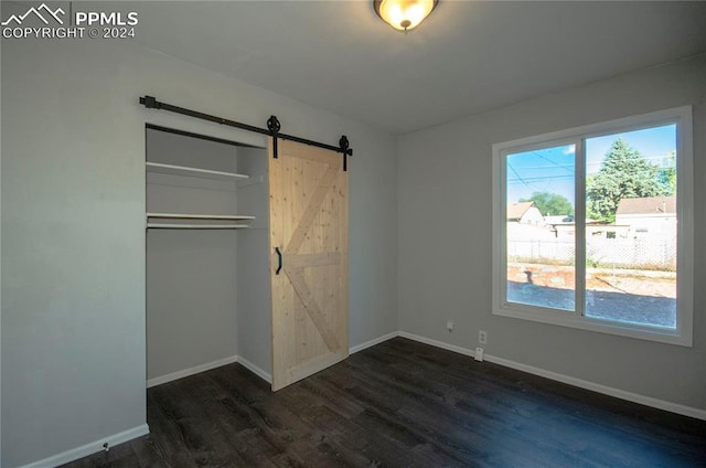 unfurnished bedroom featuring a barn door, dark hardwood / wood-style floors, and a closet