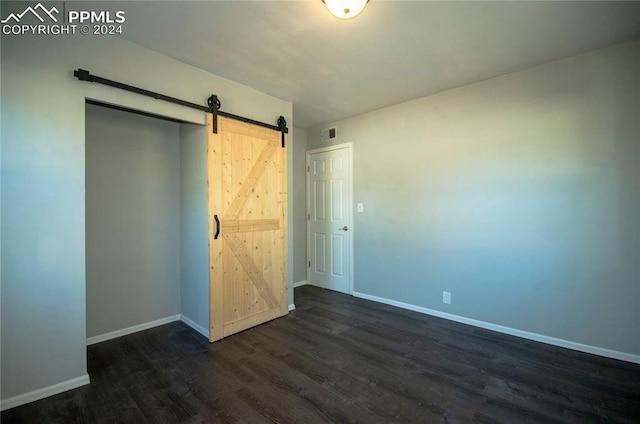 unfurnished bedroom with a barn door and dark wood-type flooring