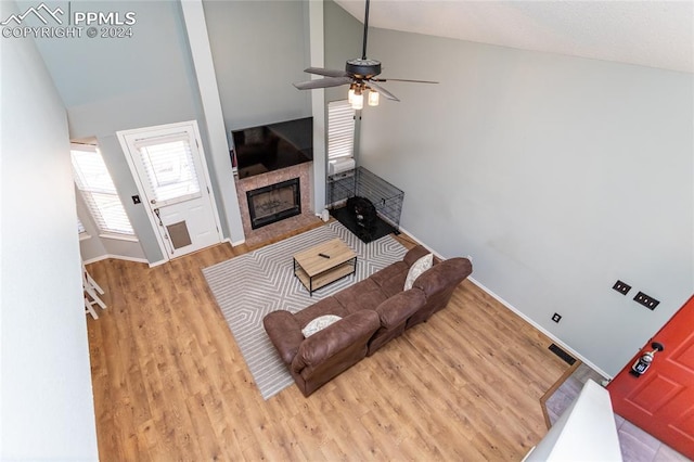 living room with a tile fireplace, light hardwood / wood-style floors, high vaulted ceiling, and ceiling fan