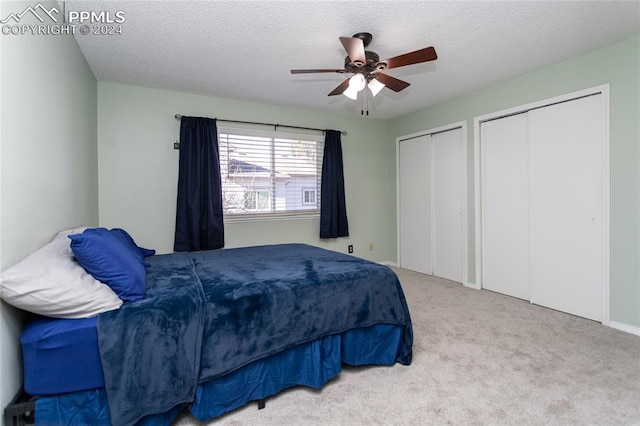 bedroom featuring carpet, ceiling fan, a textured ceiling, and multiple closets