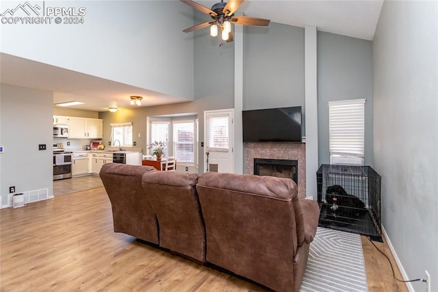 living room featuring a tile fireplace, ceiling fan, high vaulted ceiling, and light wood-type flooring