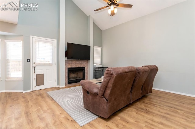 living room with high vaulted ceiling, light hardwood / wood-style flooring, ceiling fan, and a tiled fireplace