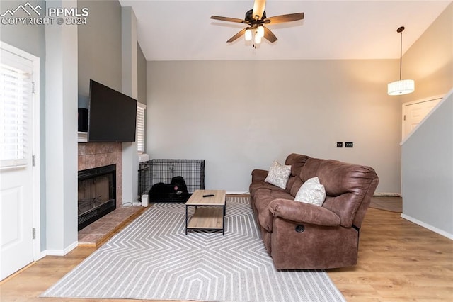 living room with a tile fireplace, ceiling fan, and light wood-type flooring