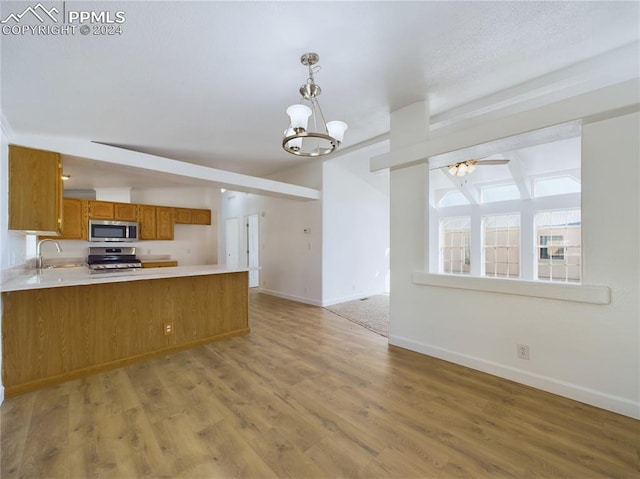 kitchen featuring kitchen peninsula, appliances with stainless steel finishes, sink, beamed ceiling, and light hardwood / wood-style floors