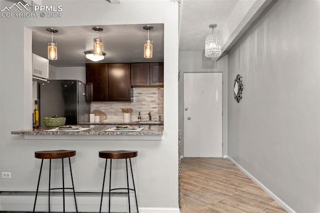 kitchen with dark brown cabinetry, sink, light hardwood / wood-style floors, stainless steel refrigerator, and a breakfast bar area