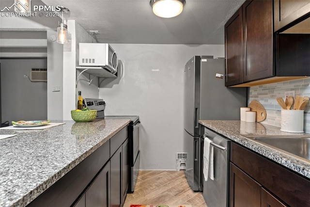 kitchen featuring pendant lighting, appliances with stainless steel finishes, dark brown cabinets, light hardwood / wood-style floors, and light stone counters