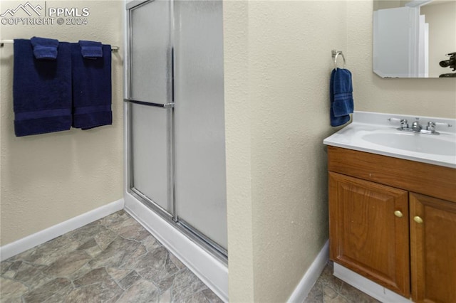 bathroom featuring a textured wall, vanity, baseboards, a shower stall, and stone finish floor