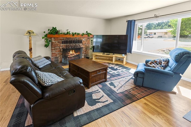 living room featuring light wood-type flooring, a stone fireplace, and baseboards