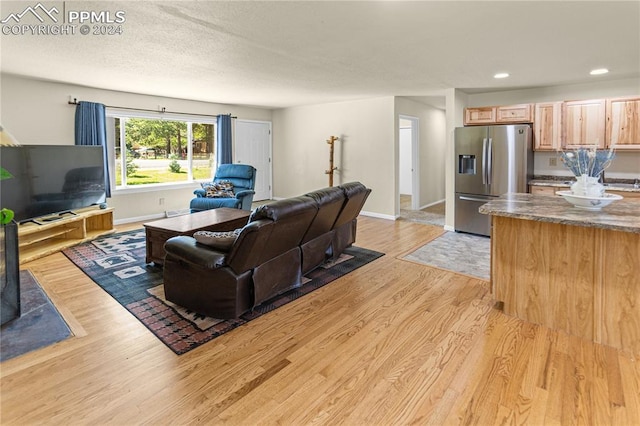 living room featuring a textured ceiling, recessed lighting, light wood-style flooring, and baseboards