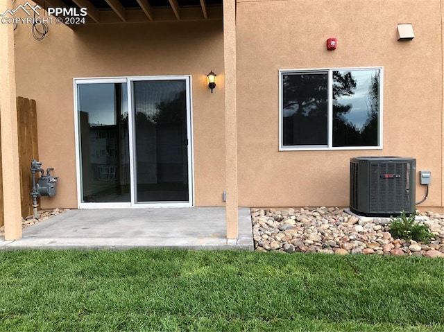 view of exterior entry featuring central AC, a patio area, and a yard