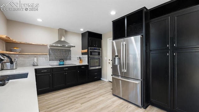 kitchen featuring sink, wall chimney range hood, tasteful backsplash, light hardwood / wood-style floors, and appliances with stainless steel finishes