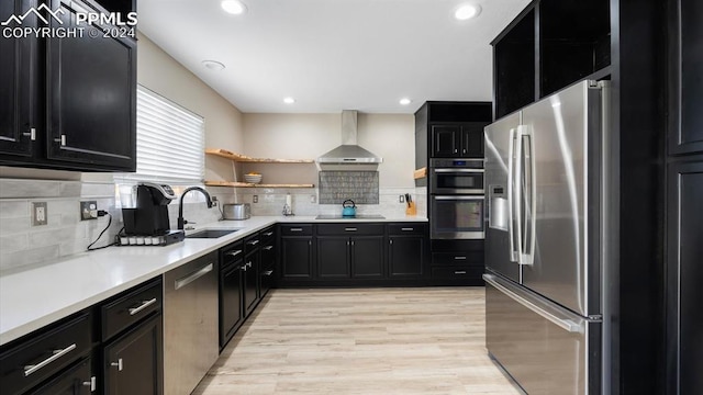 kitchen featuring decorative backsplash, appliances with stainless steel finishes, light wood-type flooring, wall chimney exhaust hood, and sink