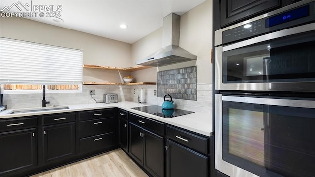 kitchen featuring sink, wall chimney range hood, light hardwood / wood-style flooring, double oven, and black electric cooktop