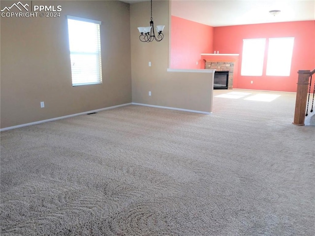 unfurnished living room featuring a fireplace, light colored carpet, an inviting chandelier, and a healthy amount of sunlight