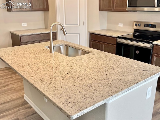 kitchen featuring light stone counters, stainless steel appliances, light hardwood / wood-style flooring, and sink