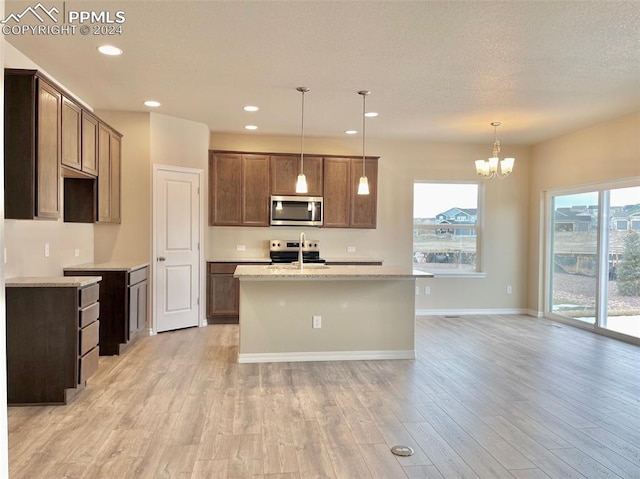 kitchen with a kitchen island with sink, light hardwood / wood-style floors, decorative light fixtures, and appliances with stainless steel finishes