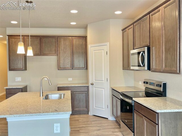 kitchen featuring sink, light stone countertops, decorative light fixtures, light hardwood / wood-style floors, and stainless steel appliances