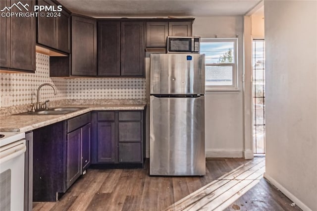 kitchen with appliances with stainless steel finishes, hardwood / wood-style flooring, light stone counters, and dark brown cabinets