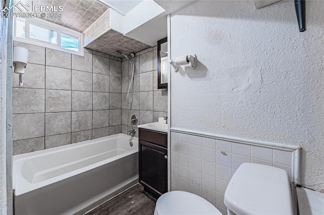 full bathroom with vanity, tiled shower / bath combo, tile walls, hardwood / wood-style floors, and toilet