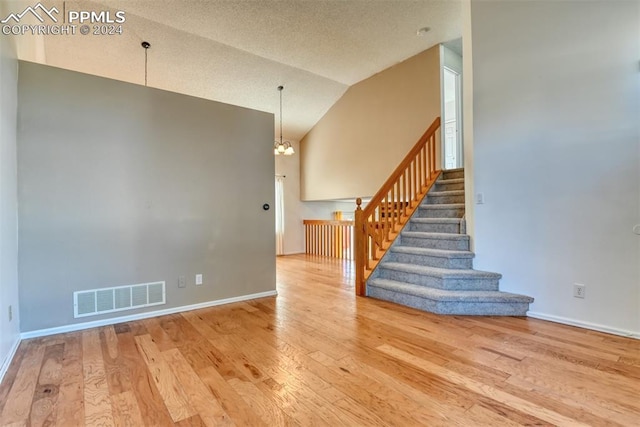 stairs with a textured ceiling, a chandelier, wood-type flooring, and vaulted ceiling