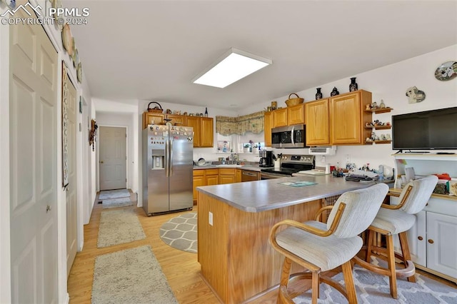 kitchen with a kitchen breakfast bar, kitchen peninsula, stainless steel appliances, and light hardwood / wood-style flooring