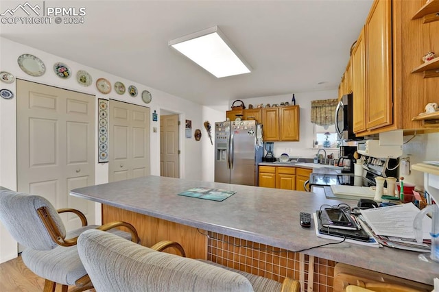 kitchen featuring sink, a kitchen breakfast bar, kitchen peninsula, appliances with stainless steel finishes, and light wood-type flooring