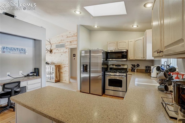 kitchen with kitchen peninsula, lofted ceiling with skylight, stainless steel appliances, and wooden walls