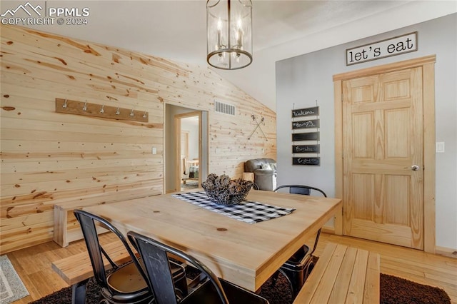 dining area featuring light hardwood / wood-style floors, an inviting chandelier, lofted ceiling, and wood walls