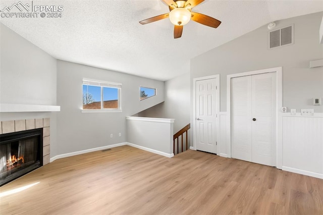 unfurnished living room with a textured ceiling, ceiling fan, a tile fireplace, light hardwood / wood-style flooring, and lofted ceiling