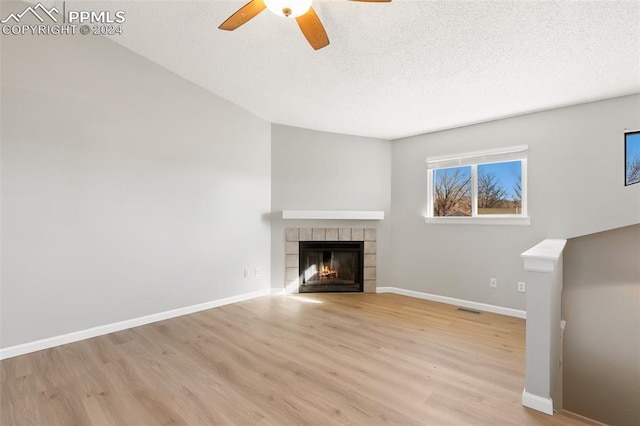 unfurnished living room with ceiling fan, a fireplace, a textured ceiling, and light wood-type flooring