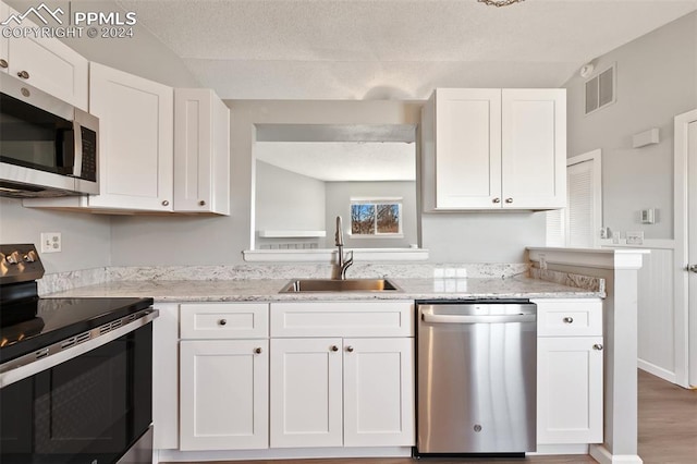 kitchen with white cabinets, appliances with stainless steel finishes, light stone counters, and sink