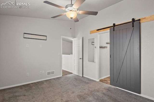 unfurnished bedroom with carpet flooring, a barn door, and ceiling fan