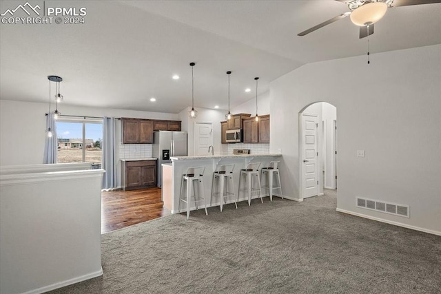 kitchen featuring a kitchen bar, hanging light fixtures, stainless steel appliances, and vaulted ceiling