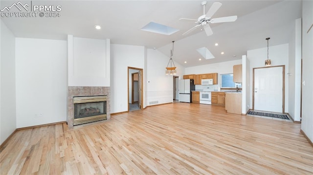 unfurnished living room featuring light wood-type flooring, a skylight, ceiling fan, high vaulted ceiling, and a tiled fireplace