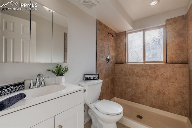 bathroom featuring a tile shower, vanity, and toilet