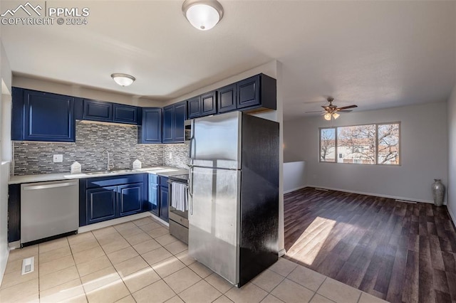 kitchen featuring appliances with stainless steel finishes, ceiling fan, sink, blue cabinetry, and light hardwood / wood-style floors