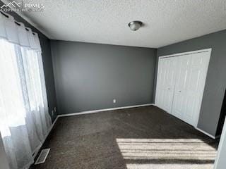 unfurnished bedroom featuring multiple windows, a textured ceiling, and dark colored carpet