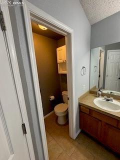 bathroom with toilet, vanity, tile patterned floors, and a textured ceiling