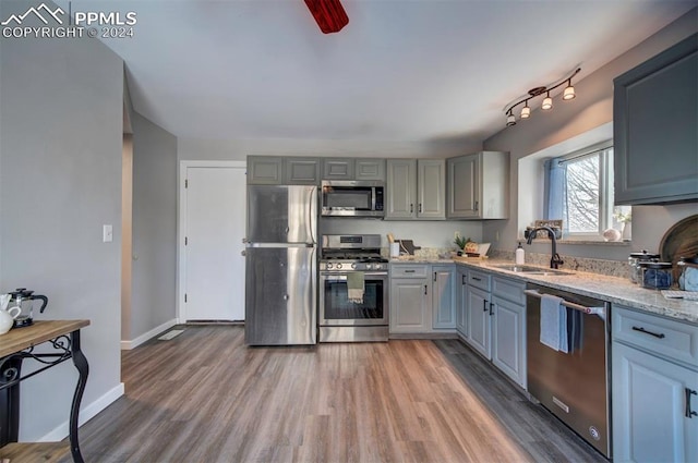 kitchen featuring sink, light stone counters, wood-type flooring, appliances with stainless steel finishes, and gray cabinets