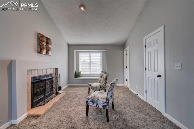 sitting room with a tiled fireplace, vaulted ceiling, carpet, and a textured ceiling