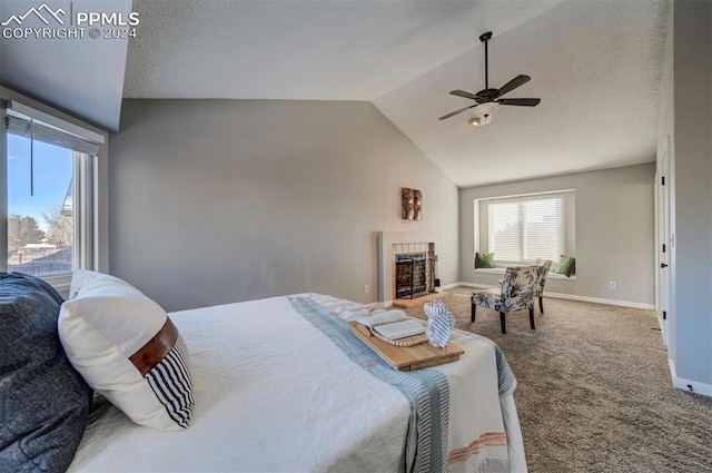 carpeted bedroom with a textured ceiling, vaulted ceiling, a tile fireplace, and ceiling fan