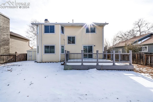 snow covered rear of property featuring a wooden deck and a storage unit