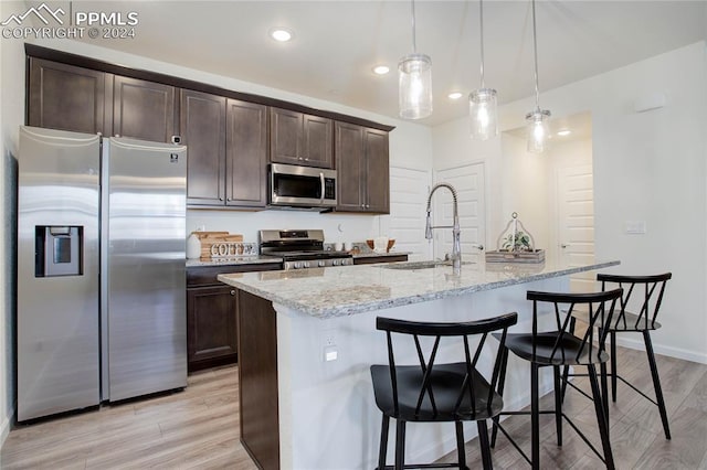 kitchen with a kitchen island with sink, sink, stainless steel appliances, and light wood-type flooring