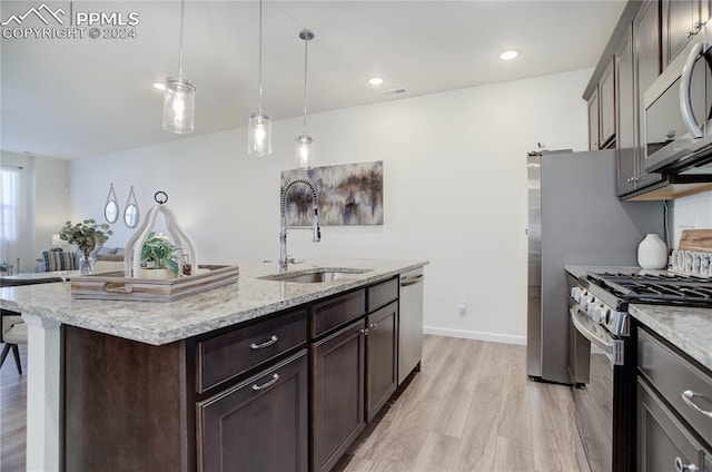 kitchen with a center island with sink, sink, decorative light fixtures, light hardwood / wood-style floors, and stainless steel appliances