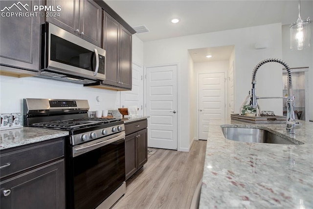 kitchen with sink, light hardwood / wood-style floors, light stone counters, dark brown cabinetry, and stainless steel appliances