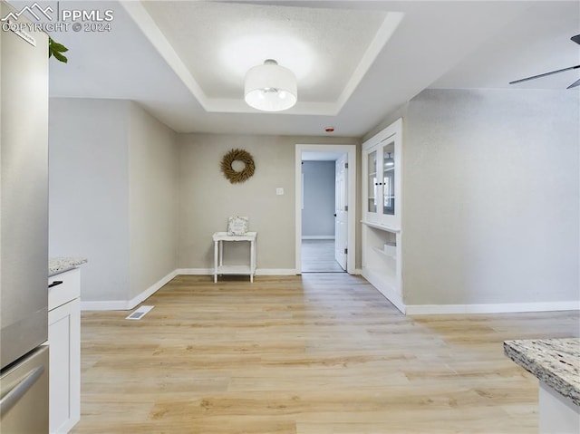 unfurnished dining area featuring light hardwood / wood-style floors, ceiling fan, and a tray ceiling