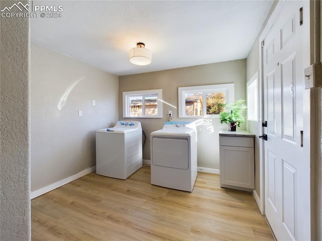 clothes washing area with cabinets, washing machine and dryer, and light hardwood / wood-style flooring