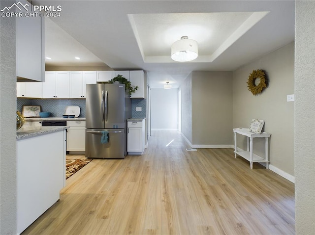 kitchen featuring white cabinets, a raised ceiling, decorative backsplash, and stainless steel refrigerator