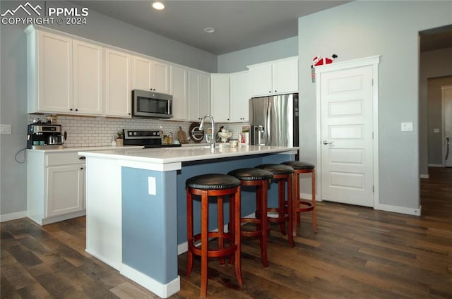 kitchen featuring a center island with sink, sink, appliances with stainless steel finishes, a kitchen bar, and white cabinetry