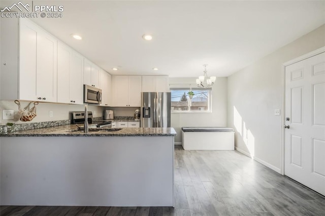 kitchen featuring stainless steel appliances, kitchen peninsula, pendant lighting, white cabinets, and hardwood / wood-style flooring